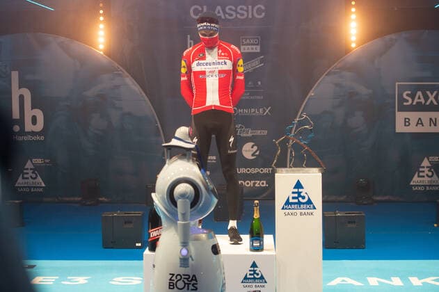 Radsport, E3 Harelbeke - Roboter führt Siegerehrung durch Kasper Asgreen (DEN DK - Deceuninck-Quick Step) gewinnt die 64. Austragung des E3-Preises und kann sich auf dem Podium feiern lassen - hier abgeschottet in der Sporthalle von Harelbeke ohne Zuschauer wegen der Covid-19 Corona Pandemie - Siegerehrung - Ehrung - Auszeichnung - Zeremonie - Zelebrierung - Ceremony - Jubel - Freude - Luck - Emotion - Emotionen - Mimik - Mimic - Gestik - Gestic - Querformat quer horizontal Event Veranstaltung: 64. E3 Saxo Bank Classic - Harelbeke nach to Harelbeke 203.9 km - Ort Location: Harelbeke - Region: West-Vlaanderen (Flandern) - Land Country: Belgien Belgium - Datum Date: 26.03.2021