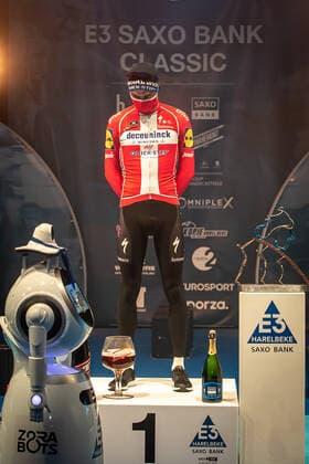 Radsport, E3 Harelbeke - Roboter führt Siegerehrung durch Kasper Asgreen (DEN DK - Deceuninck-Quick Step) bei der Siegerehrung - hier bei der Siegerzeremonie mit eigenstaendiger Uebernahme der Medaille von einem ferngesteuerten Roboter der die Ehrendamen Podiumsdamen Hostessen wegen der Covid-19 Corona Pandemie und der angemahnten Kontaktbeschraenkungen ersetzt - hier abgeschottet in der Sporthalle von Harelbeke ohne Zuschauer wegen der Covid-19 Corona Pandemie - Podium - Siegerehrung - Ehrung - Auszeichnung - Zeremonie - Zelebrierung - Ceremony - Jubel - Freude - Luck - Emotion - Emotionen - Mimik - Mimic - Gestik - Gestic - Hochformat hoch hochkant vertikal Event Veranstaltung: 64. E3 Saxo Bank Classic - Harelbeke nach to Harelbeke 203.9 km - Ort Location: Harelbeke - Region: West-Vlaanderen (Flandern) - Land Country: Belgien Belgium - Datum Date: 26.03.2021