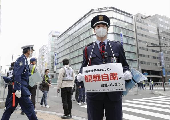 Athletics: Olympic marathon test event A security guard wearing a face mask asks pedestrians not to gather to watch a half-marathon race being held amid the coronavirus pandemic at the venue of the Tokyo Olympics marathon as a test event in the northern Japan city of Sapporo on May 5, 2021. 