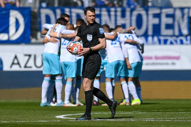 Felix Zwayer (Schiedsrichter) läuft mit dem Ball vor den sich motivierenden Schalker Spieler, 13.03.2022, Ingolstadt (Deutschland), Fussball, 2. Bundesliga, FC Ingolstadt 04 - FC Schalke 04, DFB DFL REGULATIONS PROHIBIT ANY USE OF PHOTOGRAPHS AS IMAGE SEQUENCES AND OR QUASI-VIDEO.