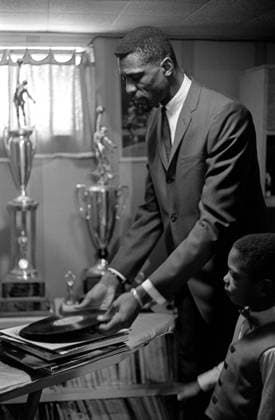 Bill Russell 13 December 1963, Boston - Basketball Feature - Bill Russell - Bill Russell puts a record onto a record player as one of his sons watches - Photo: Gerry Cranham Offside. Boston USA *** Bill Russell 13. Dezember 1963, Boston Basketball Feature Bill Russell Bill Russell legt eine Schallplatte auf einen Plattenspieler, während einer seiner Söhne zusieht Foto Gerry Cranham Abseits Boston USA  Copyright: xGerryxCranhamx xOffsidexOffside