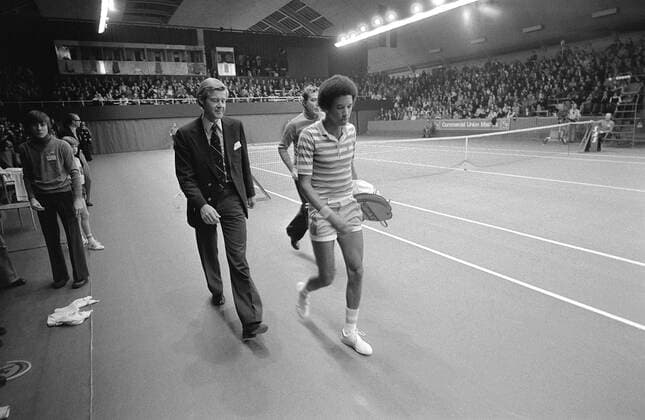 STOCKHOLM 1975-11-30. Arthur Ashe, USA, lämnar banan i vredesmod i protest mot sin rumänske motstandare Ilie Nastases uppträdande. Överdomaren Horst Klosterkemper försöker förgäves övertala Ashe att fortsätta matchen under tennisturneringen Masters i Kungliga tennishallen. Bada spelarna diskas men dagen efter ändras domslutet och Ashe döms som segrare. Stockholm Sverige TENNIS x7x