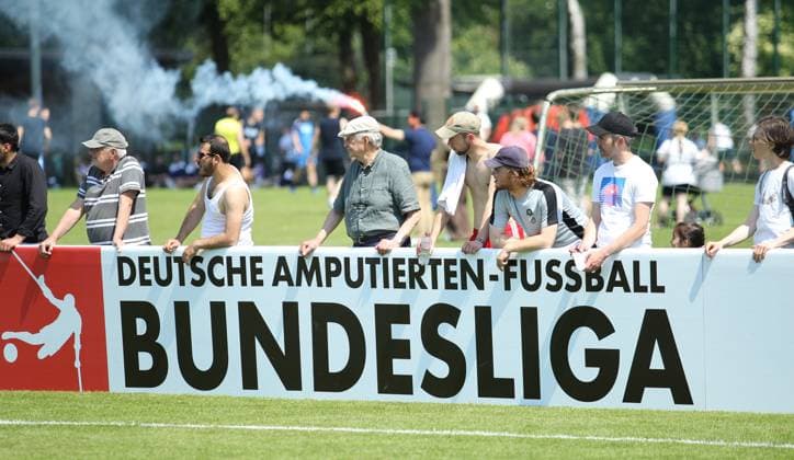 Deutsche Amputierten-Fußball Bundesliga, Dritter Spieltag auf der Paul-Hauenschild-Anlage des HSV. SG Nord-Ost - Anpfiff Hoffenheim. Zuschauer verfolgen die Partie hinter einer Werbebande der Deutschen Amputierten-Fußball Bundesliga. Norderstedt Schleswig-Holstein