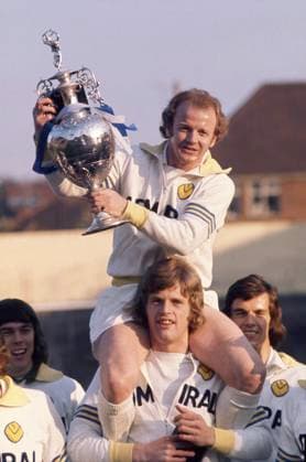 Football - 1974 1975 Leeds United Photocall Leeds United captain Billy Bremner holds the League Division One Championship Trophy wearing Admiral kit on the shoulders of Gordon McQueen with Joe Jordan right, Winners for the 1973 74 season 