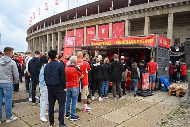 Fussball, Herren, Saison 2023 2024, UEFA Champions League (Gruppe C, 2. Spieltag), 1. FC Union Berlin - Sporting Braga, v. l. Das Stadion ist in rot gehüllt, da der 1. FC Union Berlin im Olympiastadion spielt - Zuschauer stehen vor einem Stand für Fanartikel, 03.10. 2023, Copyright: xMatthiasxKochx
