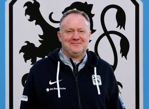 München, Deutschland 12. Dezember 2023: Fussball, Herren, 3.Liga, Saison 2023 2024, TSV 1860 München ! Achtung Fotomontage ! Hier im Bild Frank Schmöller, Schmoeller, Interimstrainer, Trainer (TSV 1860 München) Kopf,Portrait, Oberkörper, im Hintergrund das Logo des Vereins