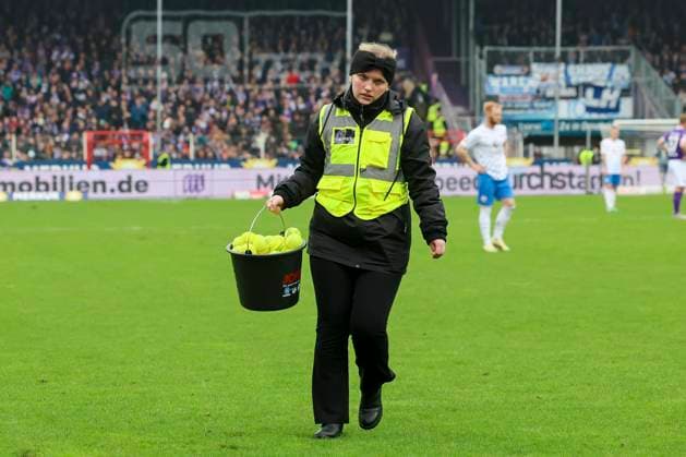 Eine Ordnerin laeuft mit einem Eimer voll Tennisbaellen ueber den Rasen, 2. Bundesliga, VfL Osnabrueck vs Hansa Rostock, Bremer Bruecke, 11.02.2024, Osnabrueck, Deutschland.