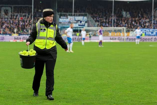 Eine Ordnerin laeuft mit einem Eimer voll Tennisbaellen ueber den Rasen, 2. Bundesliga, VfL Osnabrueck vs Hansa Rostock, Bremer Bruecke, 11.02.2024, Osnabrueck, Deutschland.