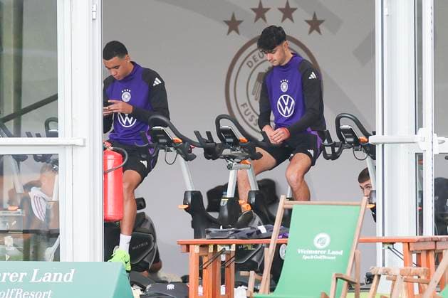 Jamal Musiala und Aleksandar Pavlovic sitzen im Zelt auf dem Fahrrad, Training der deutschen Nationalmannschaft in Blankenhain, Deutschland.