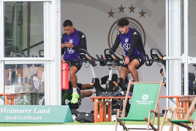 Jamal Musiala und Aleksandar Pavlovic sitzen im Zelt auf dem Fahrrad, Training der deutschen Nationalmannschaft in Blankenhain, Deutschland.