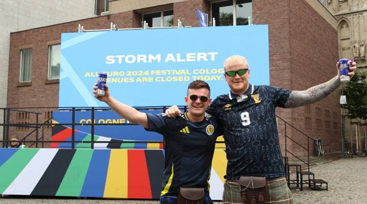 Auf einer digitalen Informationstafel teilt die Stadt Köln mit, dass wegen einer Unwetterwarnung das Fanfest zur Euro 2024 am Dienstag geschlossen bleibt. Diese beiden Fans der schottischen Fußball-Nationalmannschaft lassen sich den Spaß dennoch nicht verderben. Köln Nordrhein-Westfalen