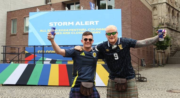 Auf einer digitalen Informationstafel teilt die Stadt Köln mit, dass wegen einer Unwetterwarnung das Fanfest zur Euro 2024 am Dienstag geschlossen bleibt. Diese beiden Fans der schottischen Fußball-Nationalmannschaft lassen sich den Spaß dennoch nicht verderben. Köln Nordrhein-Westfalen