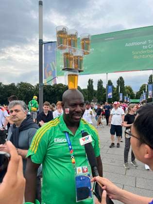 Volunteer begeistert ausländische Videoteams mit seiner Bierbecherjonglage auf dem Kopf - Köln 30.06.2024: Spanien vs. Georgien, EURO2024 M37, Achtelfinale, EM-Arena Köln