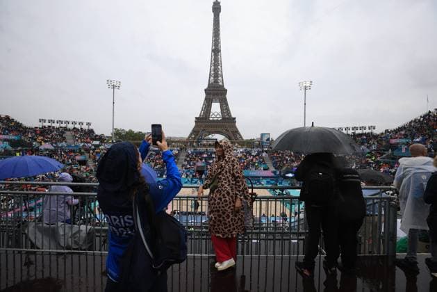 JO Paris 2024. Météo sur Volleyball de Plage (Beach Volley) JEUX OLYMPICS PARIS 2024 PHOTOPQR LE PARISIEN Olivier Arandel ; Paris ; 27 07 2024 ; 27 07 2024 - Paris -JO Paris 2024 - Épreuves de Volleyball de plage (Beach Volley) - Vue sur la Tour Eiffel sous une météo pluvieuses - (USA - CUBA) Partain Benesh (en blanc) contre Diaz Alayo (en bleu)- Arena Champs de Mars - Site de la Tour Eiffel - Les spectateurs ont enfilé les vêtements de pluie dans les gradins du stade de la Tour Eiffel LP Olivier Arandel - The Paris 2024 Summer Olympic Games, Olympische Spiele, Olympia, OS (Jul 26-Aug 11, 2024). Beach volleyball, Beachvolleyball - MEN S PRELIMINARY PHASE - POOL D MATCH 10 USE VS CUBA
