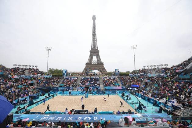 Sport Bilder des Tages JO Paris 2024. Météo sur Volleyball de Plage (Beach Volley) JEUX OLYMPICS PARIS 2024 PHOTOPQR LE PARISIEN Olivier Arandel ; Paris ; 27 07 2024 ; 27 07 2024 - Paris -JO Paris 2024 - Épreuves de Volleyball de plage (Beach Volley) - Vue sur la Tour Eiffel sous une météo pluvieuses - (USA - CUBA) Partain Benesh (en blanc) contre Diaz Alayo (en bleu)- Arena Champs de Mars - Site de la Tour Eiffel - Les spectateurs ont enfilé les vêtements de pluie dans les gradins du stade de la Tour Eiffel LP Olivier Arandel - The Paris 2024 Summer Olympic Games, Olympische Spiele, Olympia, OS (Jul 26-Aug 11, 2024). Beach volleyball, Beachvolleyball - MEN S PRELIMINARY PHASE - POOL D MATCH 10 USE VS CUBA
