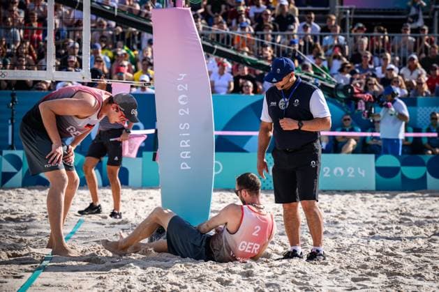 01.08.2024, Paris, Stadion Eiffelturm Beachvolleyball, Olympische Spiele, Vorrunde Clemens Wickler (GER) stolpert über Netzkamera und verletzt sich Nils Ehlers (GER) und Schiedsrichter Schiri Giovanni Bake (RSA) bei ihm