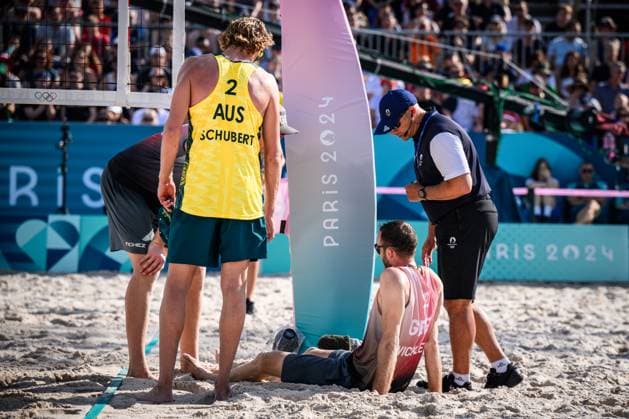 01.08.2024, Paris, Stadion Eiffelturm Beachvolleyball, Olympische Spiele, Vorrunde Clemens Wickler (GER) stolpert über Netzkamera und verletzt sich Zachery Schubert (AUS), Nils Ehlers (GER) und Schiedsrichter Schiri Giovanni Bake (RSA) bei ihm