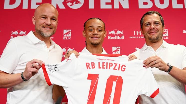 Fußball-Bundesliga Saison 2024 2025, Pressekonferenz mit Xavi Simons (Offensives Mittelfeld RB Leipzig, Rueckennummer 10), Marcel Schäfer (Geschäftsführer RB Leipzig) und Rouven Schröder (Sportdirektor RB Leipzig) (06.08.2024). Rouven Schröder (Sportdirektor RB Leipzig), Xavi Simons (Offensives Mittelfeld RB Leipzig, Rueckennummer 10) und Marcel Schäfer (Geschäftsführer Sport RB Leipzig) (v.l.n.r.) bei der Pressekonferenz von RB Leipzig (06.08.2024). Auf der PK wird die Verlängerung der Leihe von Xavi (von Paris Saint-Germain) bekanntgegeben. Schröder, Xavi und Schäfer halten ein Trikot von Xavi mit der Nummer 10 in die Höhe. Leipzig Sachsen Deutschland Red-Bull-Trainingsgelände am Cottaweg