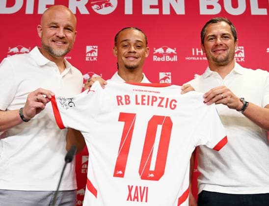 Fußball-Bundesliga Saison 2024 2025, Pressekonferenz mit Xavi Simons (Offensives Mittelfeld RB Leipzig, Rueckennummer 10), Marcel Schäfer (Geschäftsführer RB Leipzig) und Rouven Schröder (Sportdirektor RB Leipzig) (06.08.2024). Rouven Schröder (Sportdirektor RB Leipzig), Xavi Simons (Offensives Mittelfeld RB Leipzig, Rueckennummer 10) und Marcel Schäfer (Geschäftsführer Sport RB Leipzig) (v.l.n.r.) bei der Pressekonferenz von RB Leipzig (06.08.2024). Auf der PK wird die Verlängerung der Leihe von Xavi (von Paris Saint-Germain) bekanntgegeben. Schröder, Xavi und Schäfer halten ein Trikot von Xavi mit der Nummer 10 in die Höhe. Leipzig Sachsen Deutschland Red-Bull-Trainingsgelände am Cottaweg