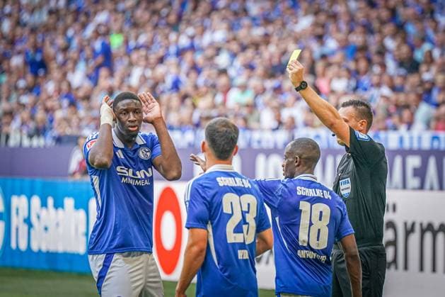 Fußball: 2. Bundesliga Saison 2024 - 2025, 4. Spieltag - FC Schalke 04 vs. 1. FC Köln - Veltins-Arena, Gelsenkirchen: Schalkes Ibrahima CissÃ Cisse bekommt von Schiedsrichter Sven Jablonski die Gelbe Karte