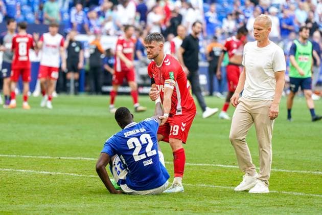 Fußball: 2. Bundesliga Saison 2024 - 2025, 4. Spieltag - FC Schalke 04 vs. 1. FC Köln - Veltins-Arena, Gelsenkirchen: Szene nach Abpfiff: Schalkes Ibrahima CissÃ Cisse ist niedergeschlagen, traurig, frustriert, enttäuscht und sitzt alleine auf dem Boden, Gegenspieler Kölns Jan Thielmann geht zu ihm hin und zieht ihn hoch - Schalkes Trainer Karel Geraerts kommt ebenfalls zu den enttäuschten Schalker Profi.