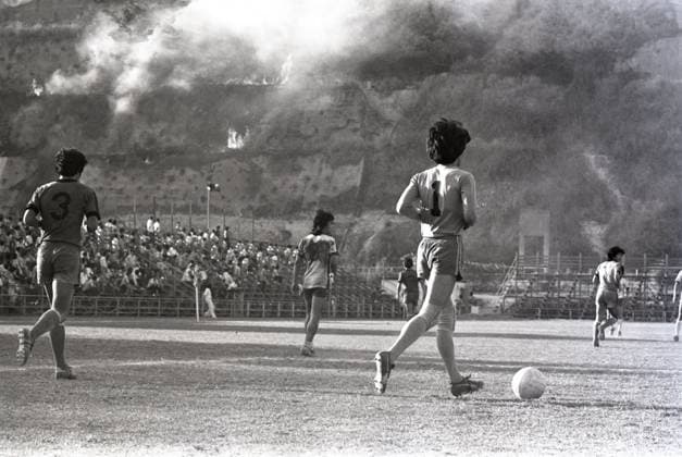 Flames and smoke rise from a scrub fire on the hillside overlooking the Boundary Street Stadium, where a heart-stopping soccer match betwen Yuen Long and Tung Sing is being held. Even the soccer players fail to concentrate on the match. 25APR77 Hong Kong Hong Kong EDITORIAL USE ONLY  Copyright: xx MER2016080116153009 RobinxLamxKitx 0795656400st