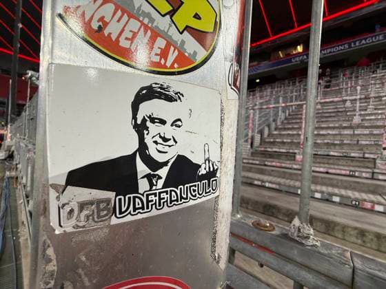 18.02.2025, Fussball UEFA Championsleague 2024 2025: Play-off Rückspiel, FC Bayern München - Celtic Glasgow, in der Allianz-Arena München. In der noch leeren Ultra-Kurve klebt ein Sticker mit dem Konterfei von Madrids Trainer Carlo Ancelotti (ITA), ein Ex-Bayern-Trainer, auf der Darstellung mit Stinkefinger und Italienischem Schmäh-Gruß an den DFB: Vaffangulo