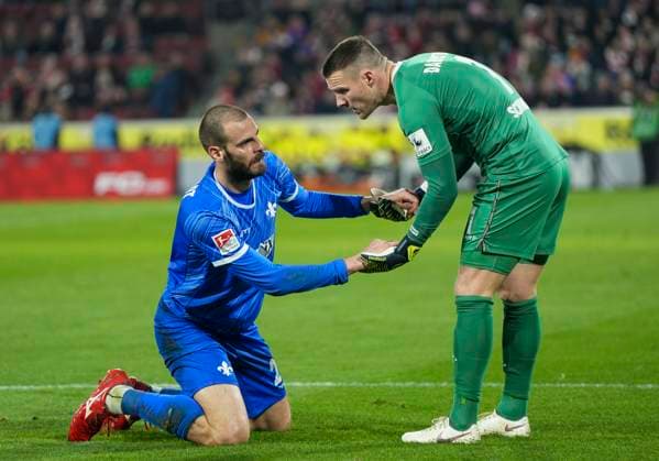 Aleksandar Vukotic (SV Darmstadt, 20) liegt nach einem Zweikampf auf dem Boden. Marcel Schuhen (SV Darmstadt, 1) hilft ihm hoch. 1. FC Köln - SC Darmstadt 98, 15.03.2025 Fussball, 2. Bundesliga, RheinEnergieStadion Köln DFL regulations prohibit any use of photographs as image sequences and or quasi-video.