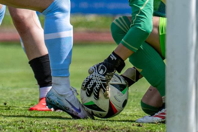 27.04.2025, Fußball, 2. Frauen-Bundesliga, 2024 2025, 23. Spieltag, FC Bayern München U 20 - SG 99 Andernach Torhüterin hält den Ball mit den Torwarthandschuhen fest, während die Stürmerin mit dem Fuß gegen den Ball tritt. Aschheim Sportpark Aschheim Bayern Deutschland