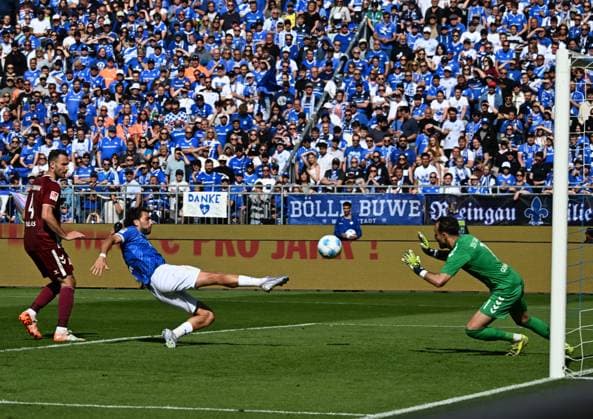 18.05.2025, xsltx, Fussball 2.Bundesliga, SV Darmstadt 98 - Jahn Regensburg v.l. Mit einer artistischen Grätsche spitzelt Fraser Hornby (SV Darmstadt 98) den Ball zum 2:1 ins Netz. Li. Florian Ballas (SSV Jahn Regensburg), re. Felix Gebhardt (SSV Jahn Regensburg) (DFL DFB REGULATIONS PROHIBIT ANY USE OF PHOTOGRAPHS as IMAGE SEQUENCES and or QUASI-VIDEO)