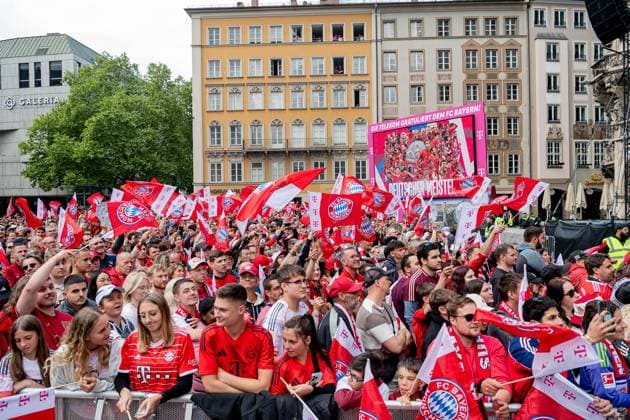 Die Fans warten auf dem Marienplatz gespannt auf die Teams. Dahinter ein Plakat mit der Aufschrift: Die Telekom gratuliert dem FC Bayern! Deutscher Meister! Empfang und Meisterehrung FC Bayern Muenchen Maenner und Frauen, Fussball, Bundesliga, Saison 2024 2025, 18.05.2025. Empfang und Meisterehrung FC Bayern Muenchen Maenner und Frauen, Fussball, Bundesliga, Saison 2024 2025, 18.05.2025. Muenchen Copyright: xEibner-Pressefoto HeikexFeinerx EP_HFR