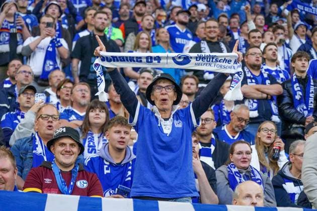 Deutschland: Fussball 2. Bundesliga 2025 26, 11. Spieltag - FC Schalke 04 vs Hertha BSC - VELTINS Arena Gelsenkirchen: Schalke 04-Fans auf der Tribüne, ein älterer Anhänger mit Schal Schalke 04 jubelt mit erhobenen Armen, umgeben von weiteren Fans in Blau-Weiß, emotionale Stimmung, Ruhrpott-Fußballleidenschaft, Heimspiel-Atmosphäre.