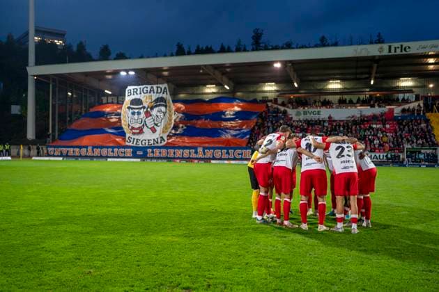 Die Mannschaft von Sportfreunde Siegen schwört sich im Kreis vor dem Spiel ein. Im Hintergrund ist die Choreo der Fans von Siegen zu sehen Sportfreunde Siegen - VfL Bochum U21, U 21 26.09.2025 Fussball, Regionalliga West, 10. Spieltag, GER, Siegen, Leimbachstadion Siegen Copyright: HMBxMedia xMarcoxBader