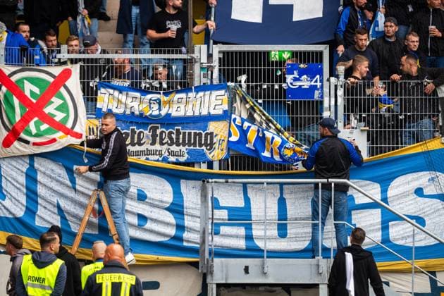 Jena , 270925, Fussball Regionalliga , FC Carl Zeiss Jena gegen Chemnitzer FC im Bild: Fans Ultras Jena Horda provozieren Spielunterbrechung indem sie zwei Fluchttore mit Transparenten und Fanen im Block versprerren