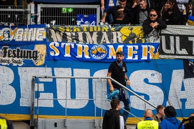 Jena , 270925, Fussball Regionalliga , FC Carl Zeiss Jena gegen Chemnitzer FC im Bild: Fans Ultras Jena Horda provozieren Spielunterbrechung indem sie zwei Fluchttore mit Transparenten und Fanen im Block versprerren stelv. Leiter der Geschäftsstelle Flori Zweigler (r.) der glechteitig Kapo der Ultras ist