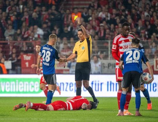 Fußball, Herren, Saison 2025 2026, 1. Bundesliga (5. Spieltag), 1. FC Union Berlin - Hamburger SV, v. l. Miro Muheim (Hamburger SV) foulte Oliver Burke (1. FC Union Berlin), er sieht von Schiedsrichter Deniz Aytekin die gelbe Kate und bedankt sich, 28.09.2025, Copyright: xMatthiasxKochx