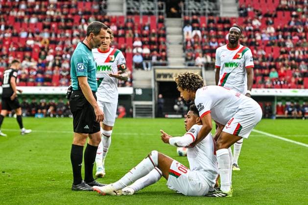 GER, 1. FBL, FC Augsburg vs VfL Wolfsburg 04.10.2025, WWK-Arena, Augsburg, GER, 1. FBL, FC Augsburg vs VfL Wolfsburg, im Bild Schiedsrichter Benjamin Brand, Noahkai Banks (FC Augsburg, 40) wurde im Gesicht getroffen, Han-Noah Massengo (FC Augsburg, 4)