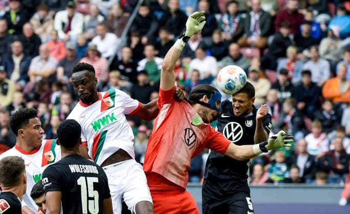 04.10.2025, xemx, Fussball 1.Bundesliga, FC Augsburg - VfL Wolfsburg v.l. Chrislain Matsima (FC Augsburg), Kamil Grabara (VfL Wolfsburg), Vini Souza (VfL Wolfsburg) Zweikampf, Aktion, action, battle for the ball (DFL DFB REGULATIONS PROHIBIT ANY USE OF PHOTOGRAPHS as IMAGE SEQUENCES and or QUASI-VIDEO) Augsburg