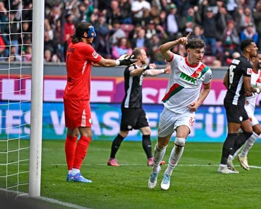 04.10.2025, Fussball 1. Bundesliga 2025 2026, 6.Spieltag, FC Augsburg - VfL Wolfsburg, in der WWK-Arena Augsburg. Mert Kömür (FC Augsburg) jubelt über das 2:0 gegen Torwart Kamil Grabara (Wolfsburg)