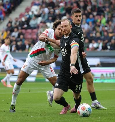 04.10.2025, 1. Bundesliga , FC Augsburg vs VfL Wolfsburg, WWK Arena Augsburg , Fussball, im Bild: Han-Noah Massengo (FC Augsburg) fault Maximilian Arnold (VfL Wolfsburg), Joakim Maehle (VfL Wolfsburg) schaut zu