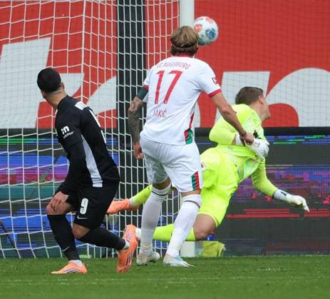 04.10.2025, 1. Bundesliga , FC Augsburg vs VfL Wolfsburg, WWK Arena Augsburg , Fussball, im Bild: Mohamed Amoura (VfL Wolfsburg) schiesst knapp daneben, Kristijan Jakic (FC Augsburg) und Finn Dahmen (FC Augsburg) geschlagen