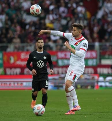 04.10.2025, 1. Bundesliga , FC Augsburg vs VfL Wolfsburg, WWK Arena Augsburg , Fussball, im Bild: Überraschend kommt ein 2: Mal auf dem Feld, Mohamed Amoura (VfL Wolfsburg) und Elvis Rexhbecaj (FC Augsburg)