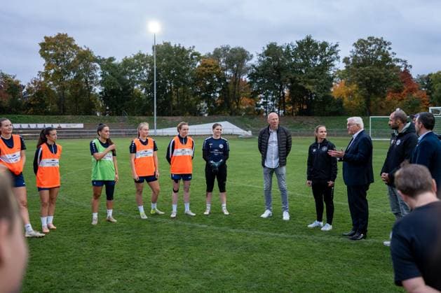 14.10.2025, GER, Besuch des Bundespräsidenten bei einem Training der Fußballerinnen der SG 99 Andernach Nach Ankunft des Bundespräsidenten Frank-Walter Steinmeier unterbrechen die Spielerinnen ihr Training und heißen ihn willkommen. Die Spielerinnen und das Staff-Team stehen in einem Kreis zusammen.