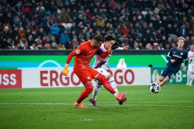 Deutschland: DFB-Pokal 2025 26, 2. Runde - FC Augsburg vs VfL Bochum - WWK Arena (Augsburg): Fabian Rieder Fabian Rieder, (FC Augsburg, 32) im Zweikampf mit Timo Horn, (VfL Bochum, 1) Augsburg WWK Arena Bayern Deutschland Copyright: xBenedictxChristx