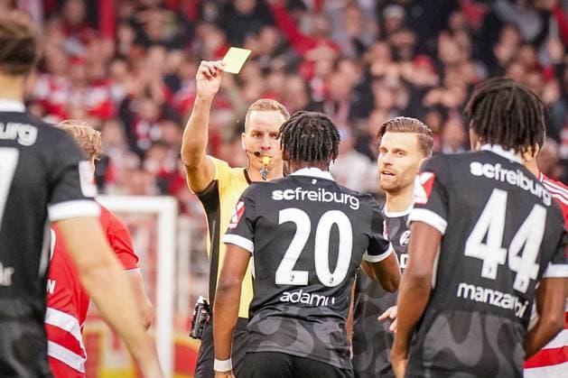 Deutschland: Fussball Bundesliga 2025 26, 9. Spieltag - 1. FC Union Berlin vs SC Freiburg - An der Alten Försterei (Berlin): Schiedsrichter Sören Storks zeigt Junior Adamu (SC Freiburg, 20) Gelbe Karte Berlin Deutschland Copyright: xJOERANxSTEINSIEKx