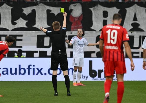 01.11.2025, xsltx, Fussball 1.Bundesliga, 1.FC Heidenheim - Eintracht Frankfurt v.l. Christian Dingert (Schiedsrichter) zeigt Arthur Theate (Eintracht Frankfurt) die gelbe Karte (DFL DFB REGULATIONS PROHIBIT ANY USE OF PHOTOGRAPHS as IMAGE SEQUENCES and or QUASI-VIDEO)