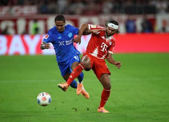 Fussball, Herren, Bundesliga, Saison 2025 2026, FC Bayern München - Bayer 04 Leverkusen, Allianz Arena Arthur (Bayer 04 Leverkusen) (li.) mit Serge Gnabry (FC Bayern München) (re.) im Zweikampf um den Ball DFB, DFL regulations prohibit any use of photographs as image sequences and or quasi-video