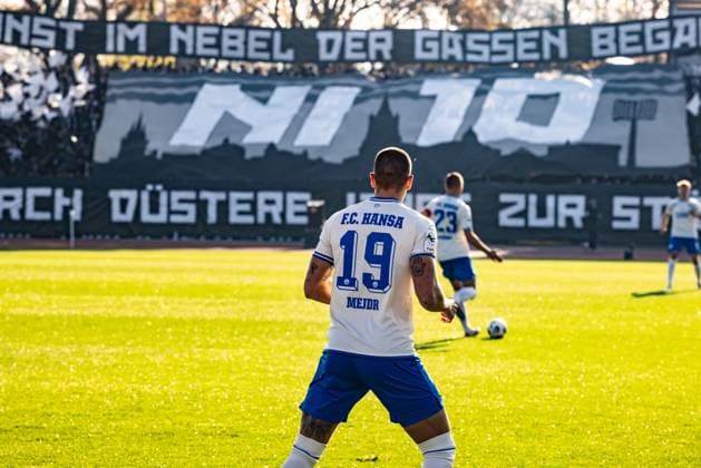 Fussball, Saison 2025 2026, 3. Liga, Donaustadion Ulm, 14. Spieltag, SSV Ulm 1846 Fußball - FC Hansa Rostock, 08.11.2025 08.11.2025, Fussball, Saison 2025 2026, 3. Liga, Donaustadion Ulm, 14. Spieltag, SSV Ulm 1846 Fußball - FC Hansa Rostock, 19 Jan Mejdr (FC Hansa Rostock), im Hintergrund: Die Fans des SSV Ulm im D-Block Donaustadion mit einer Choreo zu 15 Jahre Fangruppe Nebulosa Impero Foto: Lucca Fundel Ulm Donaustadion Baden-Württemberg Deutschland