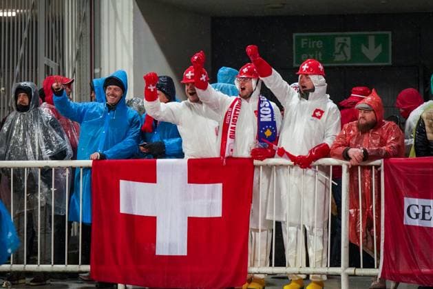 Fussball WM-Qualifikation 2025 26, 10. Spieltag Kosovo vs Schweiz Fadil-Vokrri-Stadion (Pristina): Pristina, Kosovo, Europa: Schweizer Fans im Regen, weiße Schutzanzüge, rote Helme mit Kreuz, Schweiz-Flagge, Kosovo-Schal, Auswärtssupport, starke Stimmung, Ponchos, Nässe, Wetterlage, Fußballkultur, Sicherheit, UEFA-Quali, Medienrelevanz: Fanverhalten, Regen, Matchday. Pristina Kosovo *** Football World Cup Qualification 2025 26, 10 Matchday Kosovo vs Switzerland Fadil Vokrri Stadium Pristina Pristina, Kosovo, Europe Swiss fans in the rain, white protective suits, red helmets with cross, Switzerland flag, Kosovo scarf, away support, strong atmosphere, ponchos, wet, weather conditions, soccer culture, safety, UEFA Quali, media relevance fan behavior, rain, Matchday Pristina Kosovo Copyright: xJOERANxSTEINSIEKx