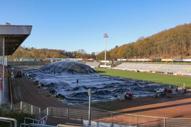 Das Leimbachstadion, Heimstaette (Heimstätte) der Sportfreunde Siegen. Vor der Haupttribuene (Haupttribüne) wird mit Waerme (Wärme), Warmer Luft unter eine Folie der Rasen aufgetaut. Es wird alles versucht, damit das Heimspiel am morgigen Samstag gegen den SC Fortuna Koeln (Köln) stattfinden kann. Fussball Regionalliga West, Leimbachstadion, Sportfreunde Siegen am 21.11.2025 in Siegen Deutschland.